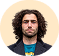 Portrait of a man with curly hair and beard wearing a blue and green shirt against a plain background.